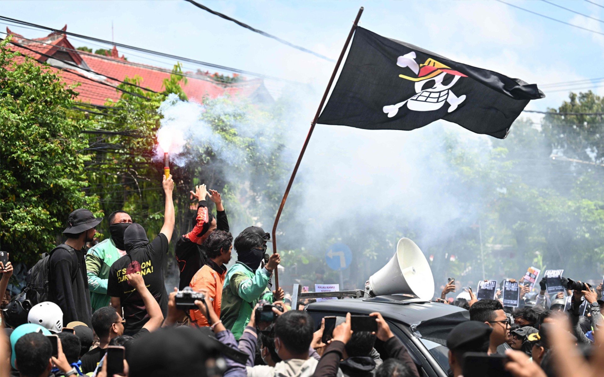 Manifestantes seguram um sinalizador e agitam uma bandeira pirata do anime japonês One Piece, uma tendência da internet usada para criticar políticas governamentais, durante uma manifestação em frente à delegacia de polícia de Bali, em Denpasar, na ilha de Bali, Indonésia, em 30 de agosto de 2025. A Indonésia foi abalada por protestos em grandes cidades, incluindo a capital Jacarta, em 29 de agosto, depois que imagens se espalharam de um motorista de mototáxi sendo atropelado por um veículo tático da polícia durante manifestações anteriores contra baixos salários e benefícios financeiros para parlamentares.