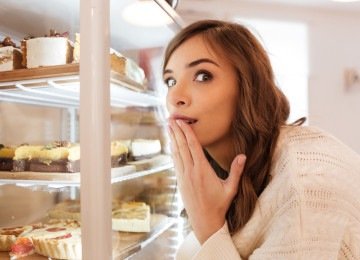 Mulher animada, em pé, em frente a vitrine de doces; imagem meramente ilustrativa -  (crédito:  Vadym Drobot/Freepik)