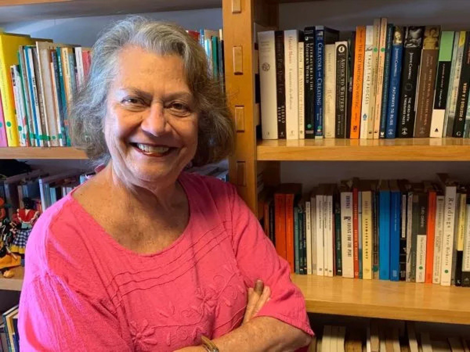 Escritora Ana Maria Machado usa blusa vermelha e sorri, em frente a estante de livros