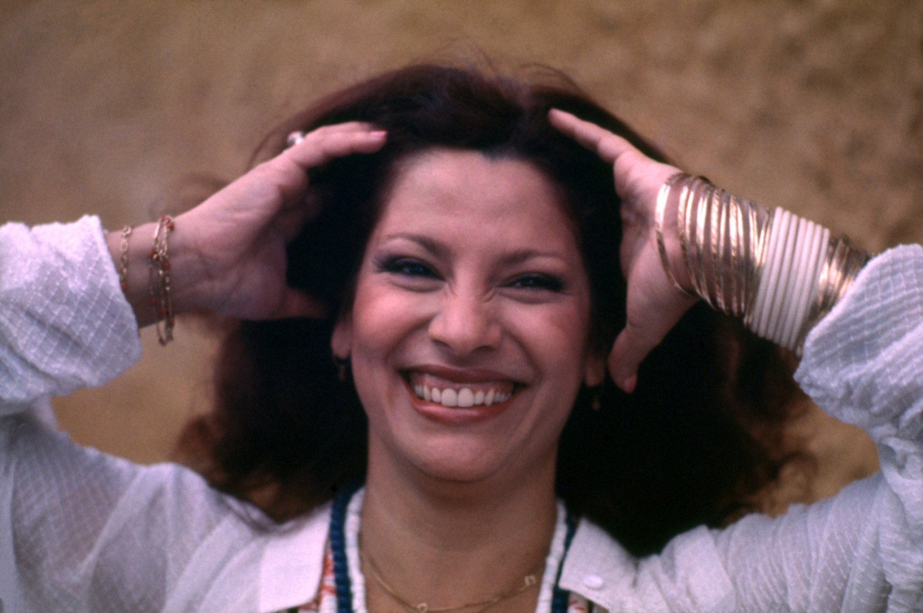 Clara Nunes sorri, olhando para a c&acirc;mera, com as duas m&atilde;os na cabe&ccedil;a