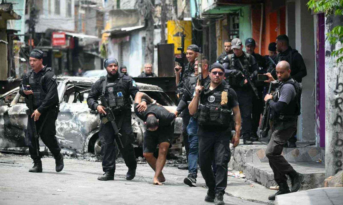 Policiais escoltam um suspeito preso durante a Operação Contenção 
para fora da favela Vila Cruzeiro, no complexo da Penha no Rio de Janeiro -  (crédito: Mauro PIMENTEL / AFP)