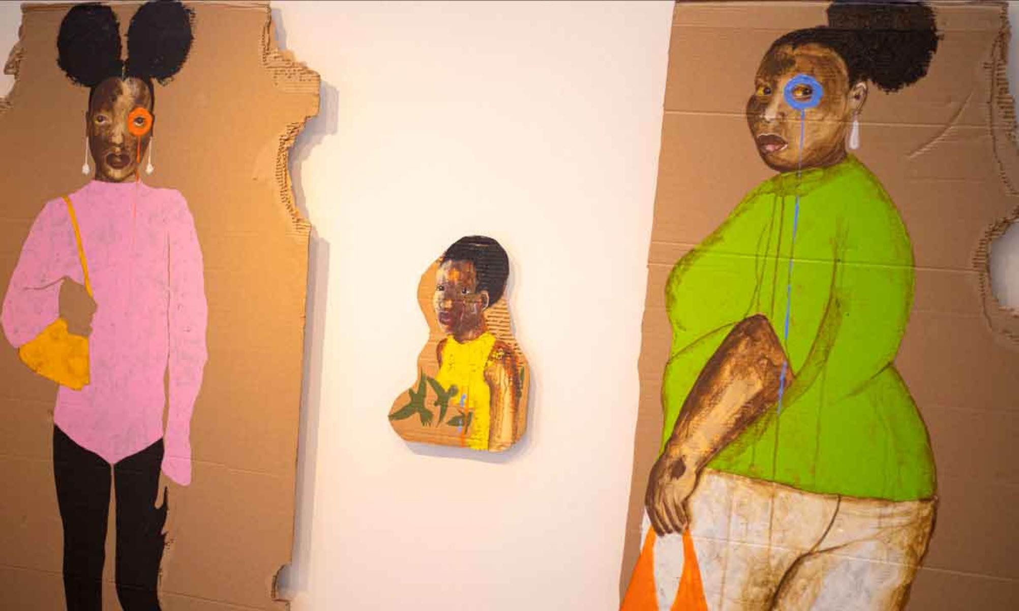 Mulheres negras e crian&ccedil;a de roupas coloridas pintadas em papel&atilde;o pelo artista Petch&oacute; Silveira