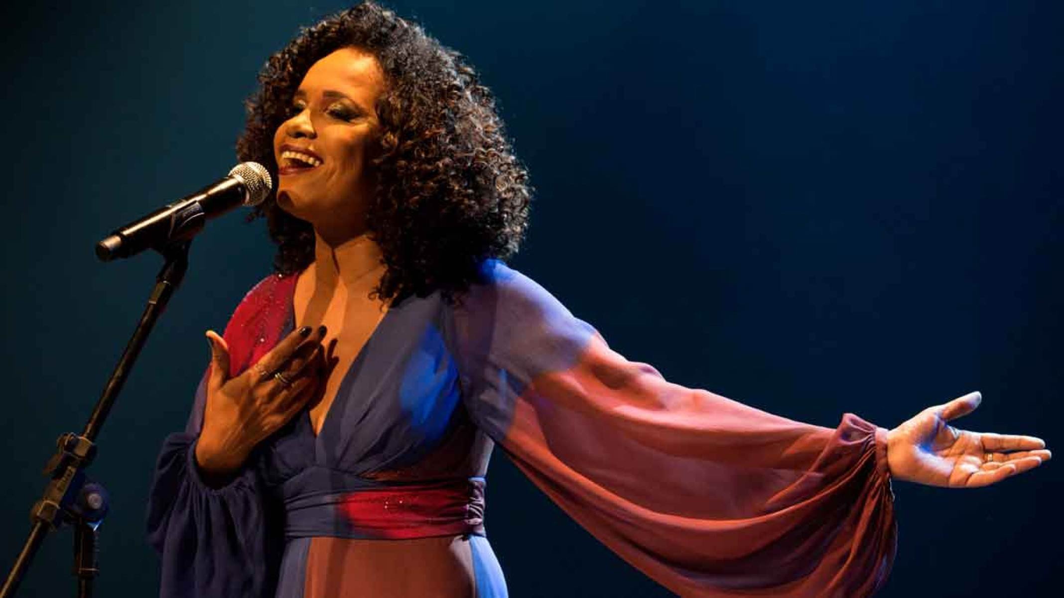 A cantora Teresa Cristina abre os bra&ccedil;os, no palco, enquanto canta
