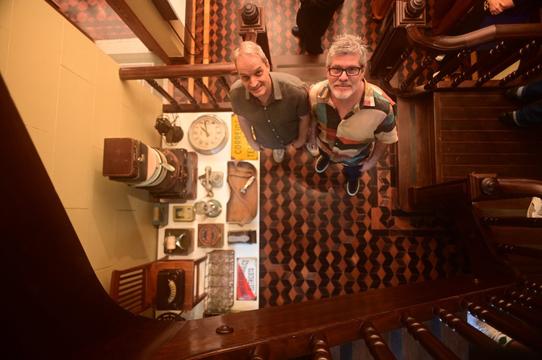  Curadores Marconi Drummond e Maurício Meireles estão lado a lado no andar de baixo do centro cultural Casa Rosada, em BH, e olham para cima
