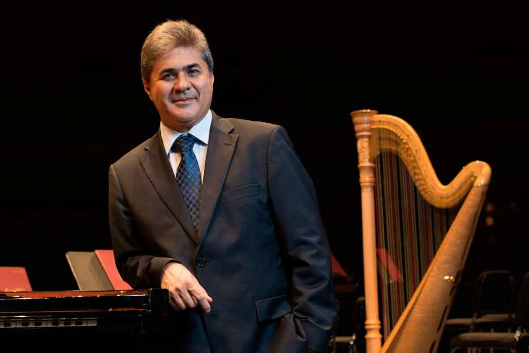 Diomar Silveira, gestor da Filarm&ocirc;nica de Minas, olha para a c&acirc;mera ao lado de uma harpa 