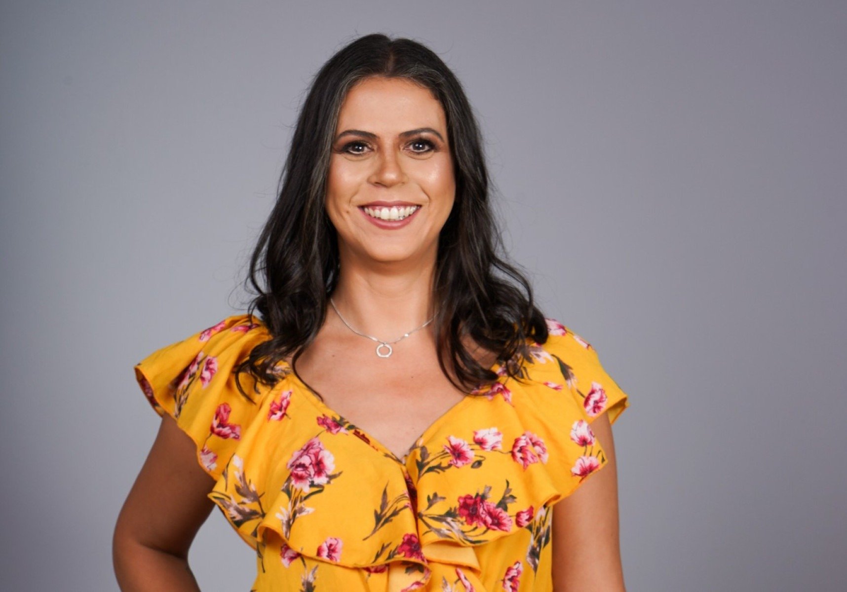 Escritora Fernanda Emediato usa vestido amarelo e olha para a c&acirc;mera, sorrindo