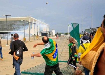 Homem vestido com bandeira do Brasil atira objeto em dire&ccedil;&atilde;o ao Pal&aacute;cio do Planalto, durante os atos de 8 de janeiro de 2023 -  (crédito: Sergio Lima / AFP)