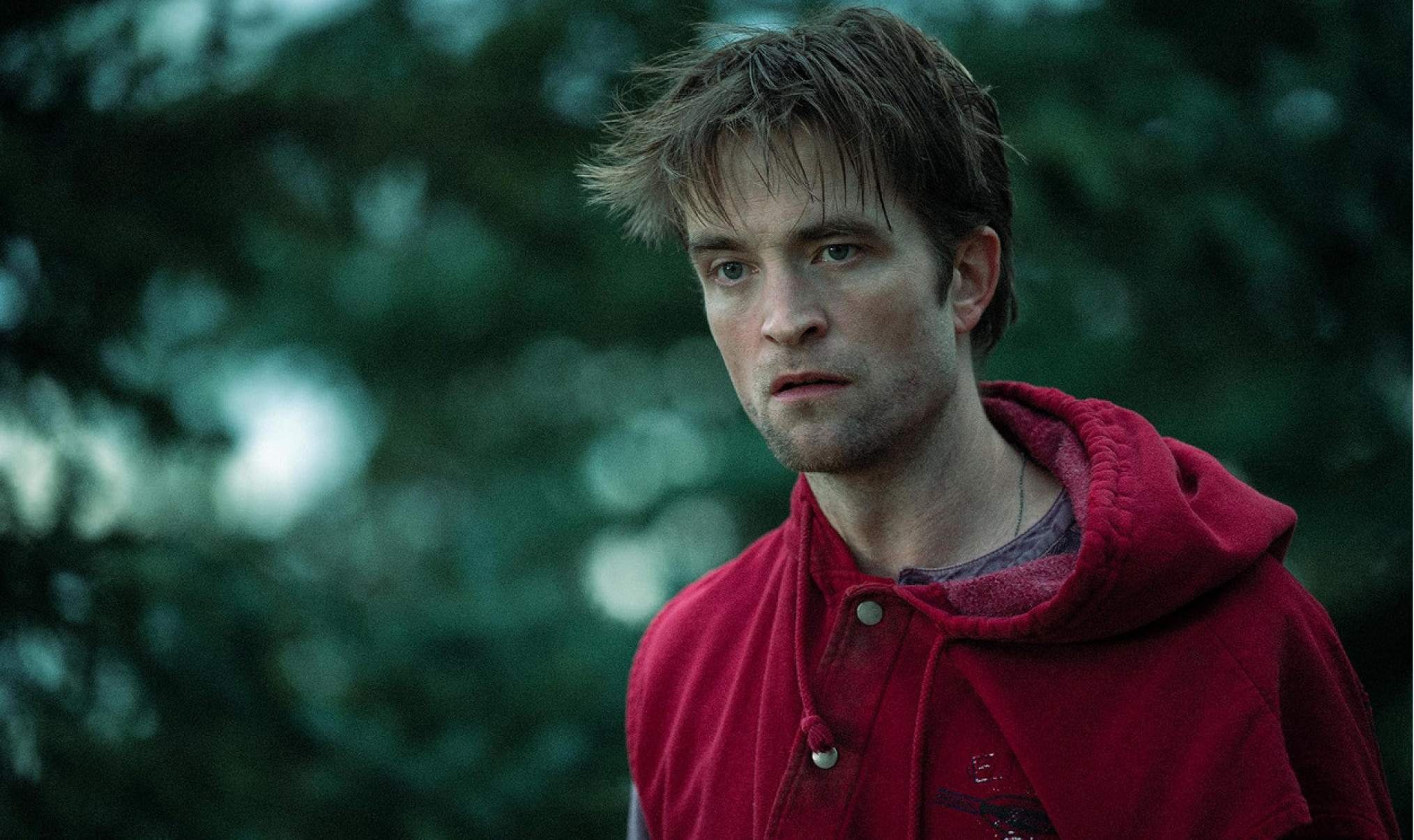 Ator Robert Pattinson tem corte no rosto, olhar tristonho e veste moletom vermelho em cena do filme Morra, amor