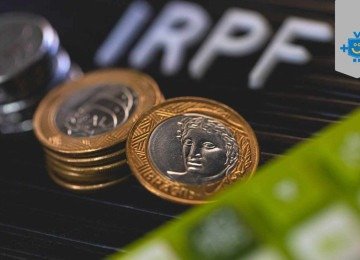 Moedas de real sobre teclado com a sigla IRPF ao fundo, representando o imposto de renda e a fiscalização financeira no Brasil. -  (crédito: Reprodução Educando seu Bolso)