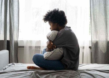 Jovem triste sentada na cama abraçada ao travesseiro; jovens enfrentam bullying e violência em tempos de redes sociais -  (crédito: Freepik)