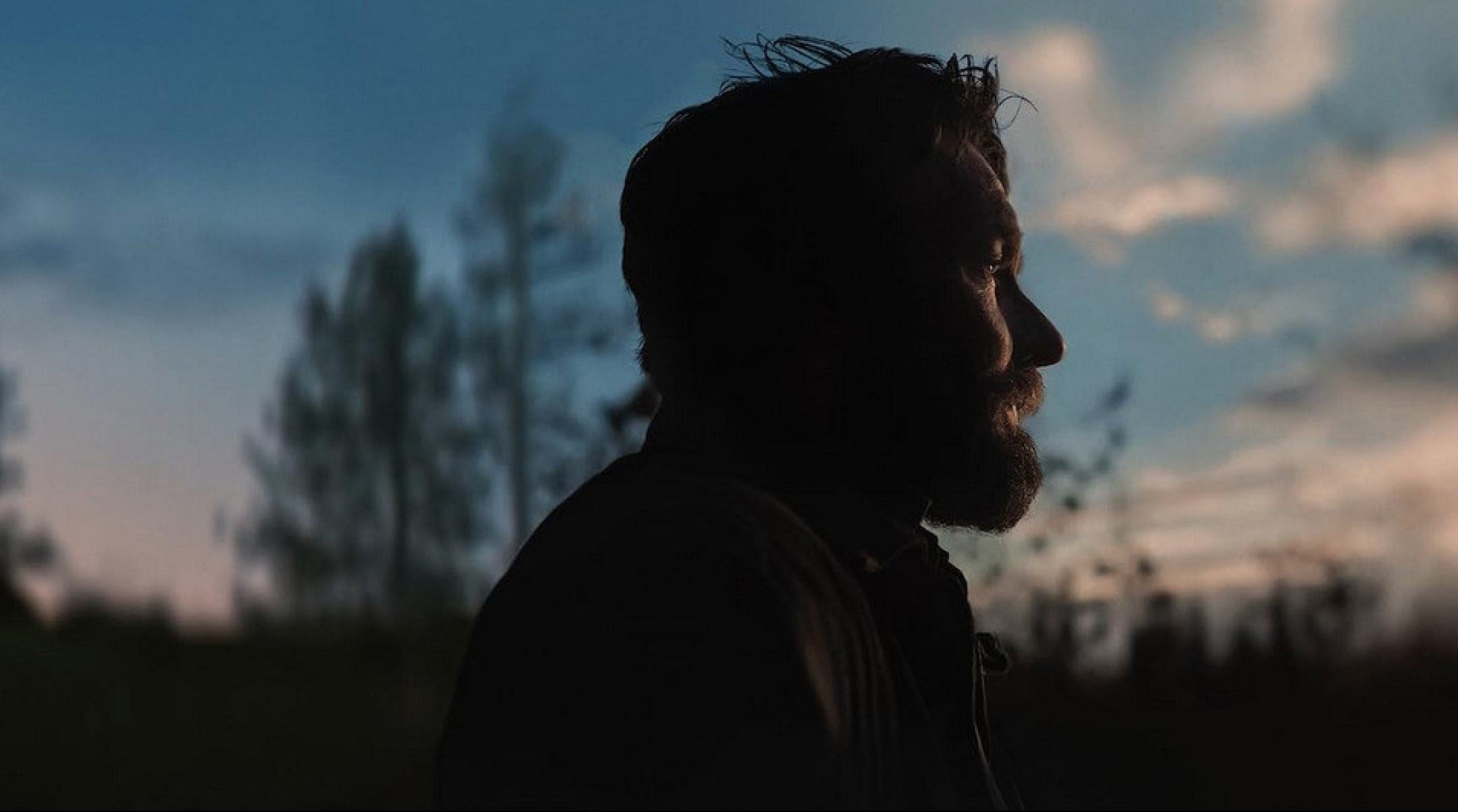 Ator Joe Edgerton est&aacute; de lado, na penumbra, tendo ao fundo o c&eacute;u azul em cena do filme Sonhos de trem