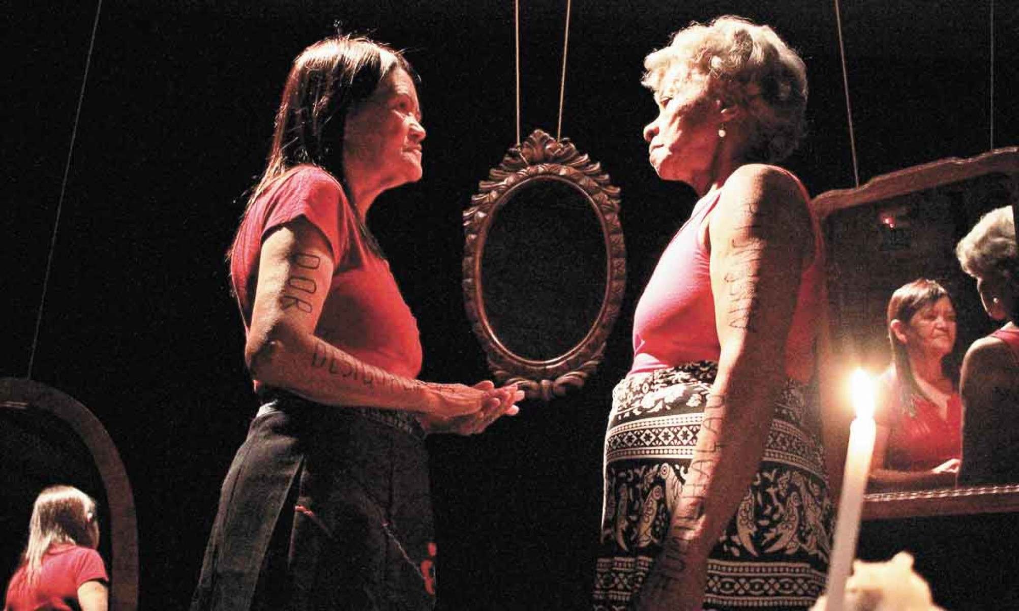 Dora e Silvana, personagens do documentário Abre alas, estão de perfil, frente a frente, em ambiente iluminado por uma vela