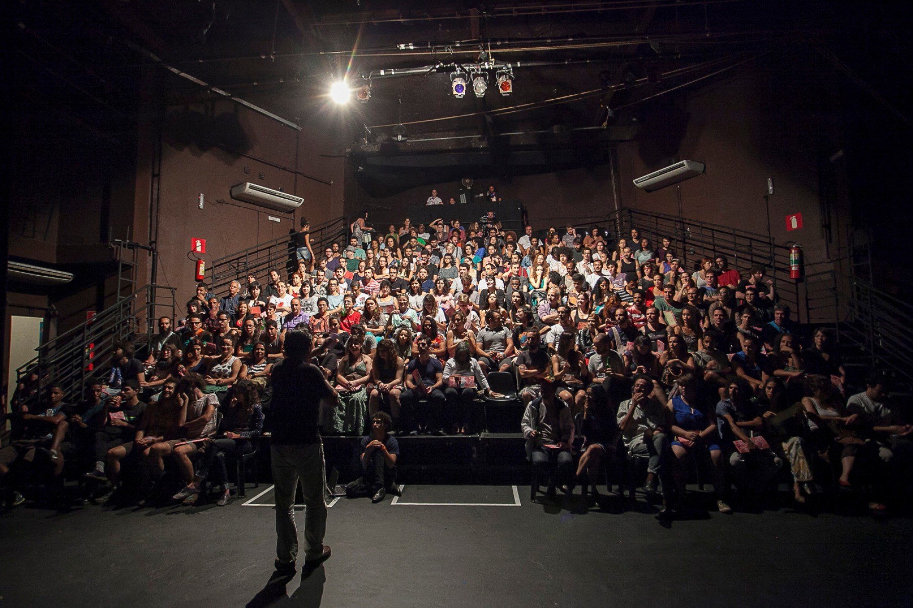 Plateia lotada do Festival Cenas Curtas, no Galp&atilde;o Cine Horto. De costas, um artista est&aacute; no palco 