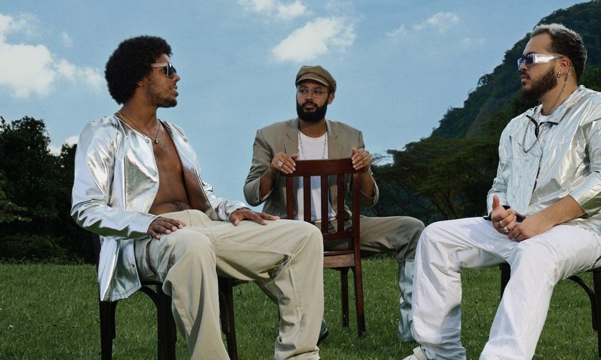  O Trio Gilsons, formado por Jos&eacute; Gil, Francisco Gil e Jo&atilde;o Gil, est&aacute; ao ar livre, sentado em cadeiras de jardim, e tem ao fundo o c&eacute;u azul