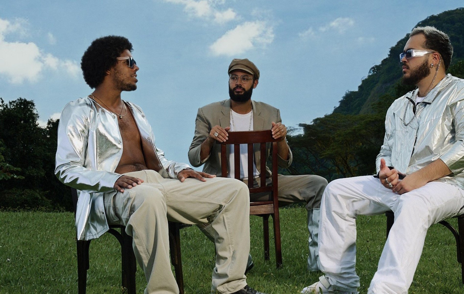  O Trio Gilsons, formado por Jos&eacute; Gil, Francisco Gil e Jo&atilde;o Gil, est&aacute; ao ar livre, sentado em cadeiras de jardim, e tem ao fundo o c&eacute;u azul