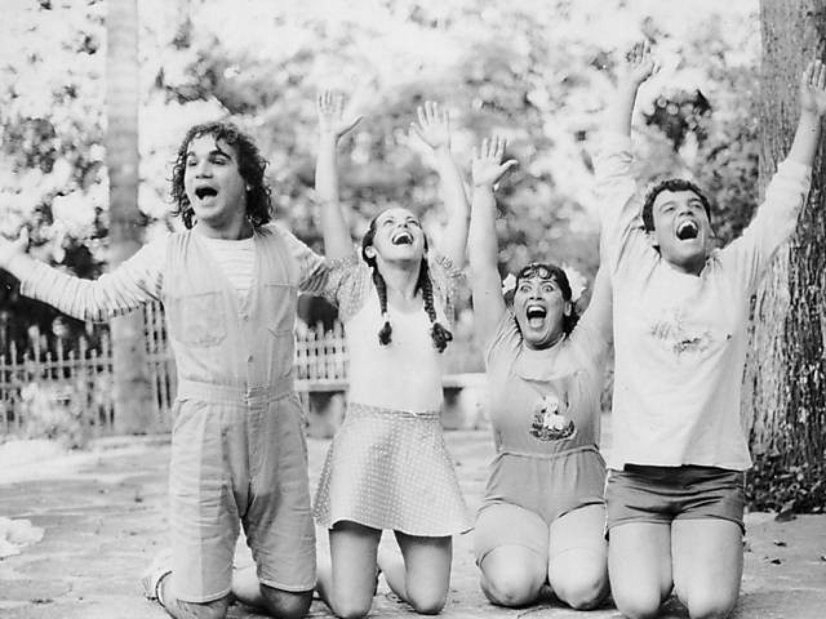 Quatro atores do Grupo Galp&atilde;o est&atilde;o ajoelhados num parque com os bra&ccedil;os para o alto