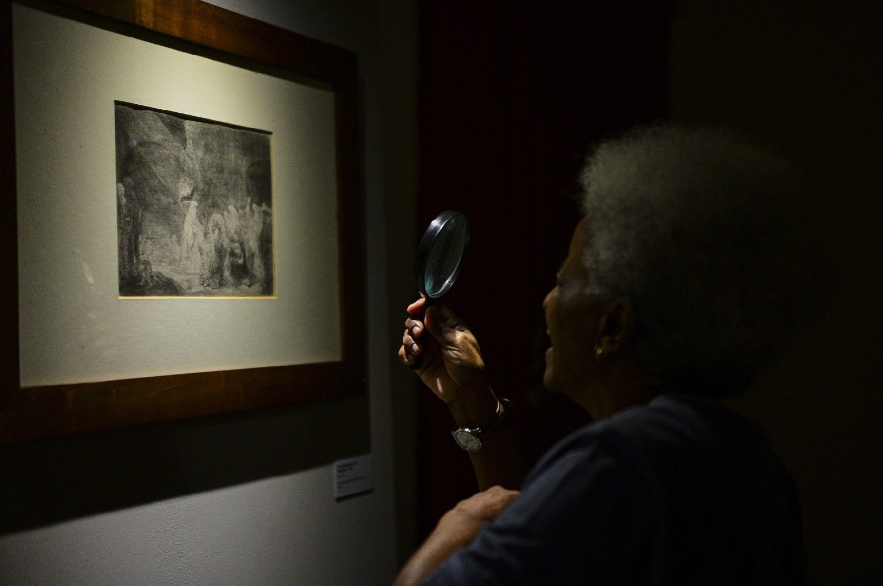 Espectadora usa lupa para ver detalhes de gravura de Rembrandt exposta na Casa Fiat, em Belo Horizonte