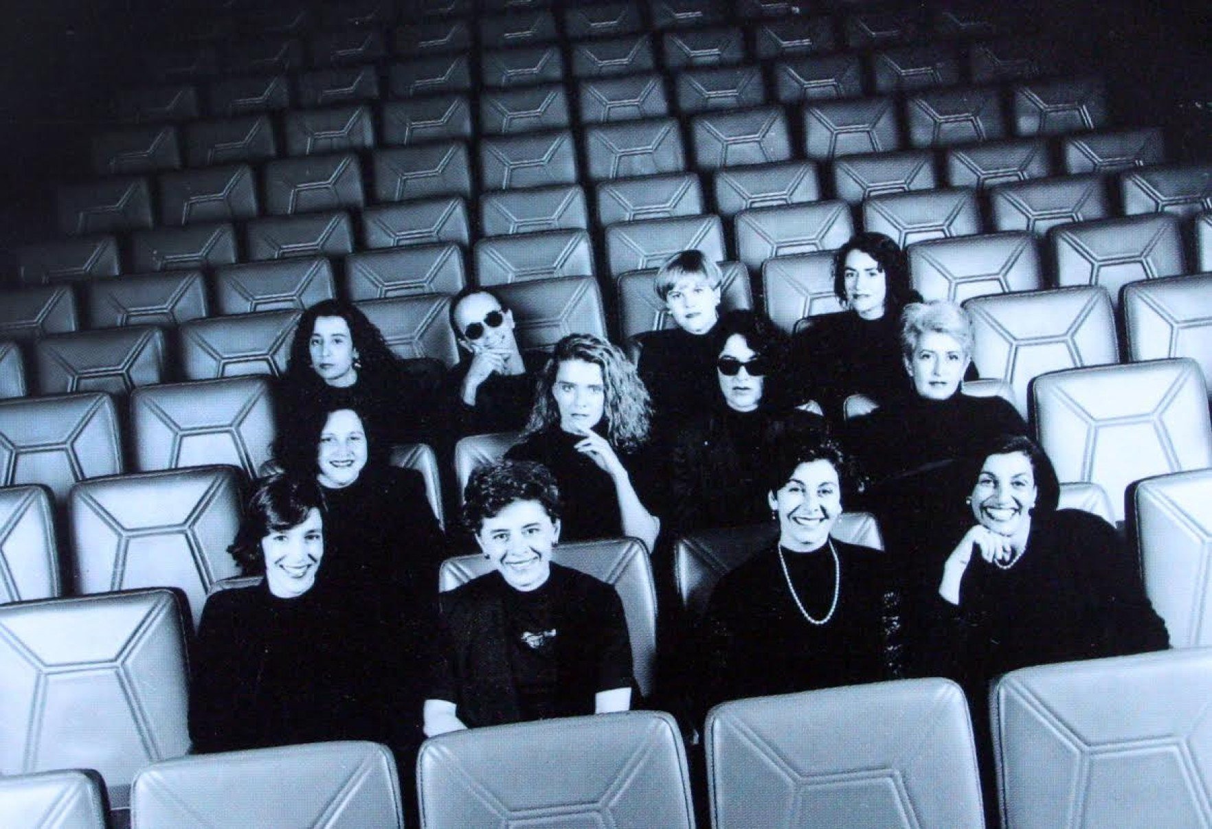 Integrantes do Grupo Mineiro de Moda vestem roupa preta e est&atilde;o sentados juntos em plateia de teatro