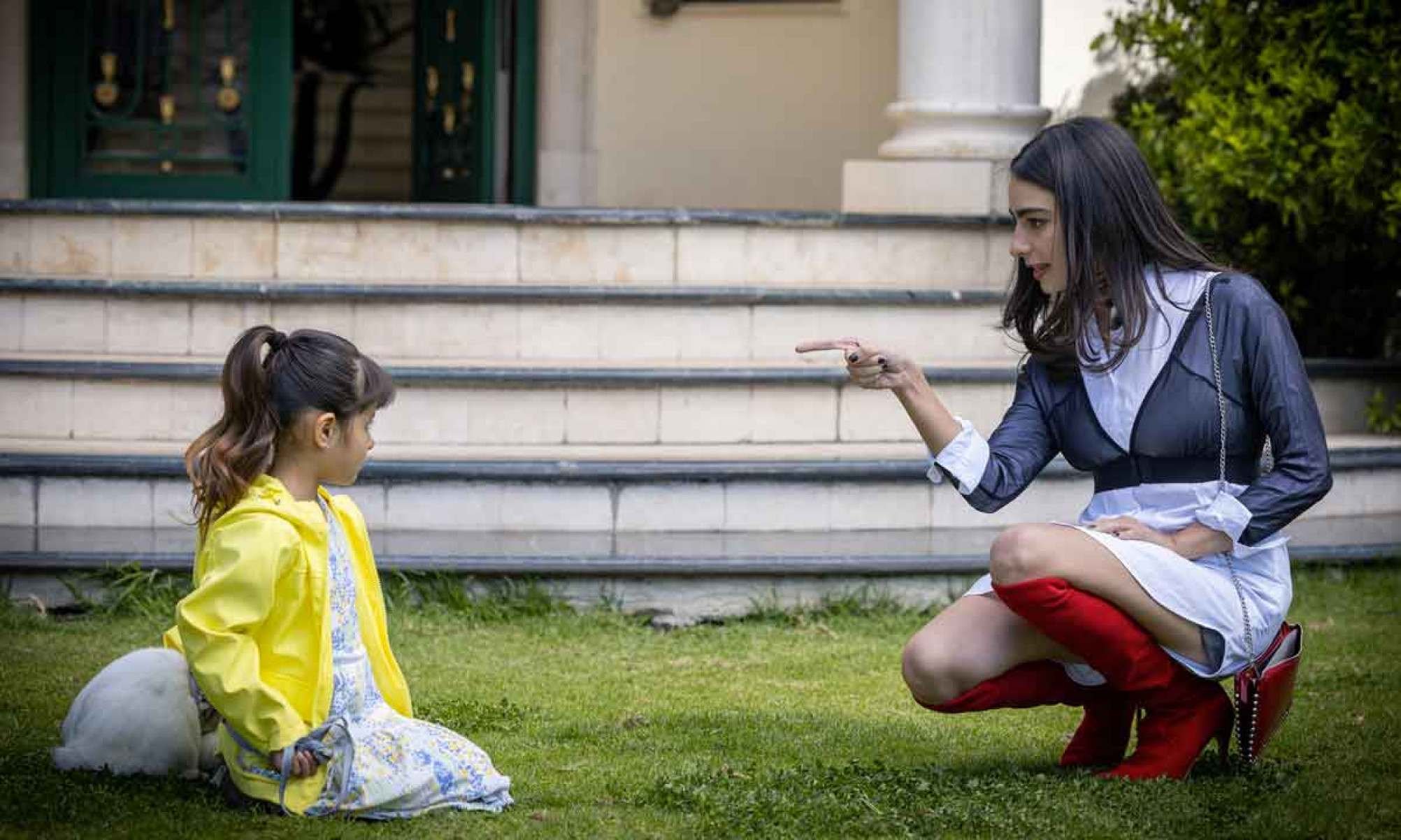 Atriz mirim Almudena L&oacute;pez est&aacute; ajoelhada na grama e olha para a atriz Valentina Buzurro, que est&aacute; brava e ralha com ela, em cena da novela Presente de amor