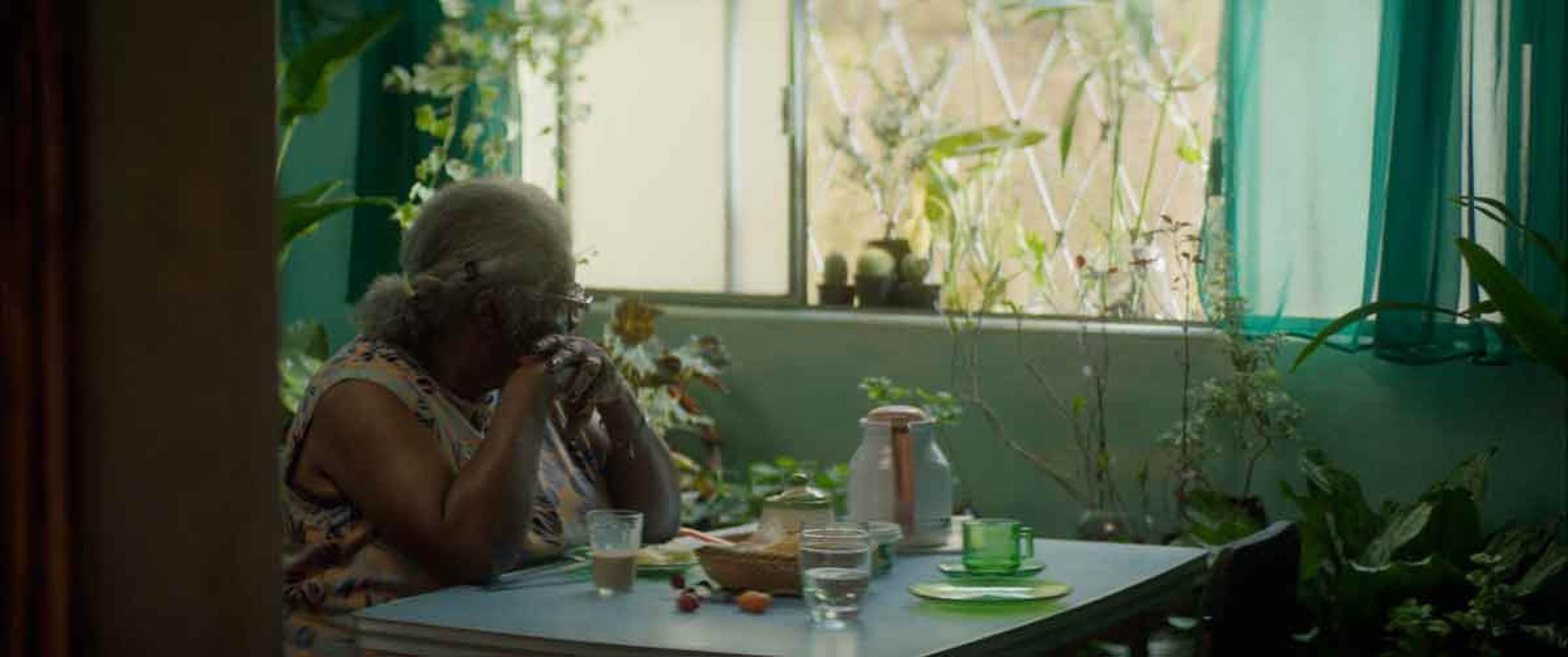 Fotografia mostra a escritora e atriz Concei&ccedil;&atilde;o Evaristo, sentada &agrave; mesa, perto de janela aberta, de perfil, em cena do filme Se eu fosse vivo, vivia