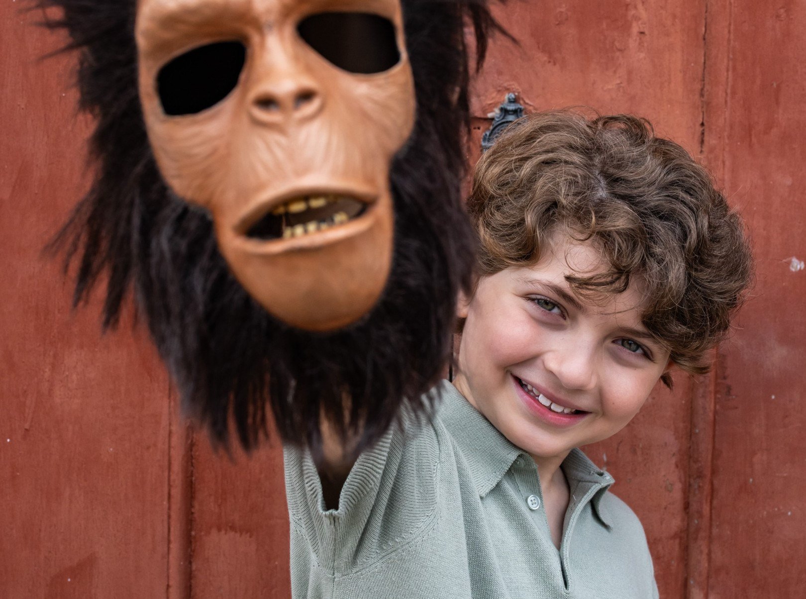Ator mirim Lorenzo Melo sorri e ergue m&aacute;scara de macaco com barba