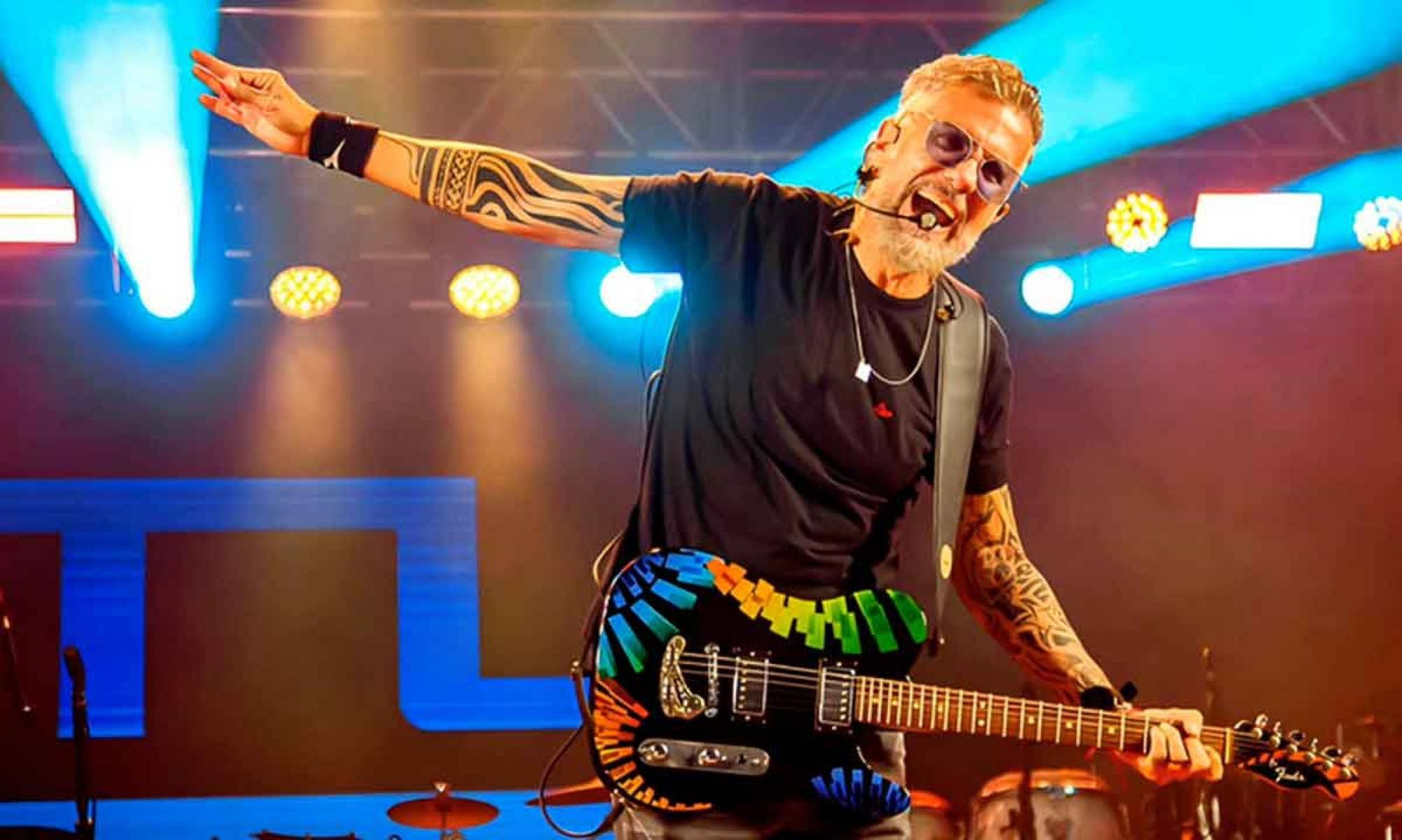 M&uacute;sico Tuca Fernandes canta no palco e segura a guitarra 