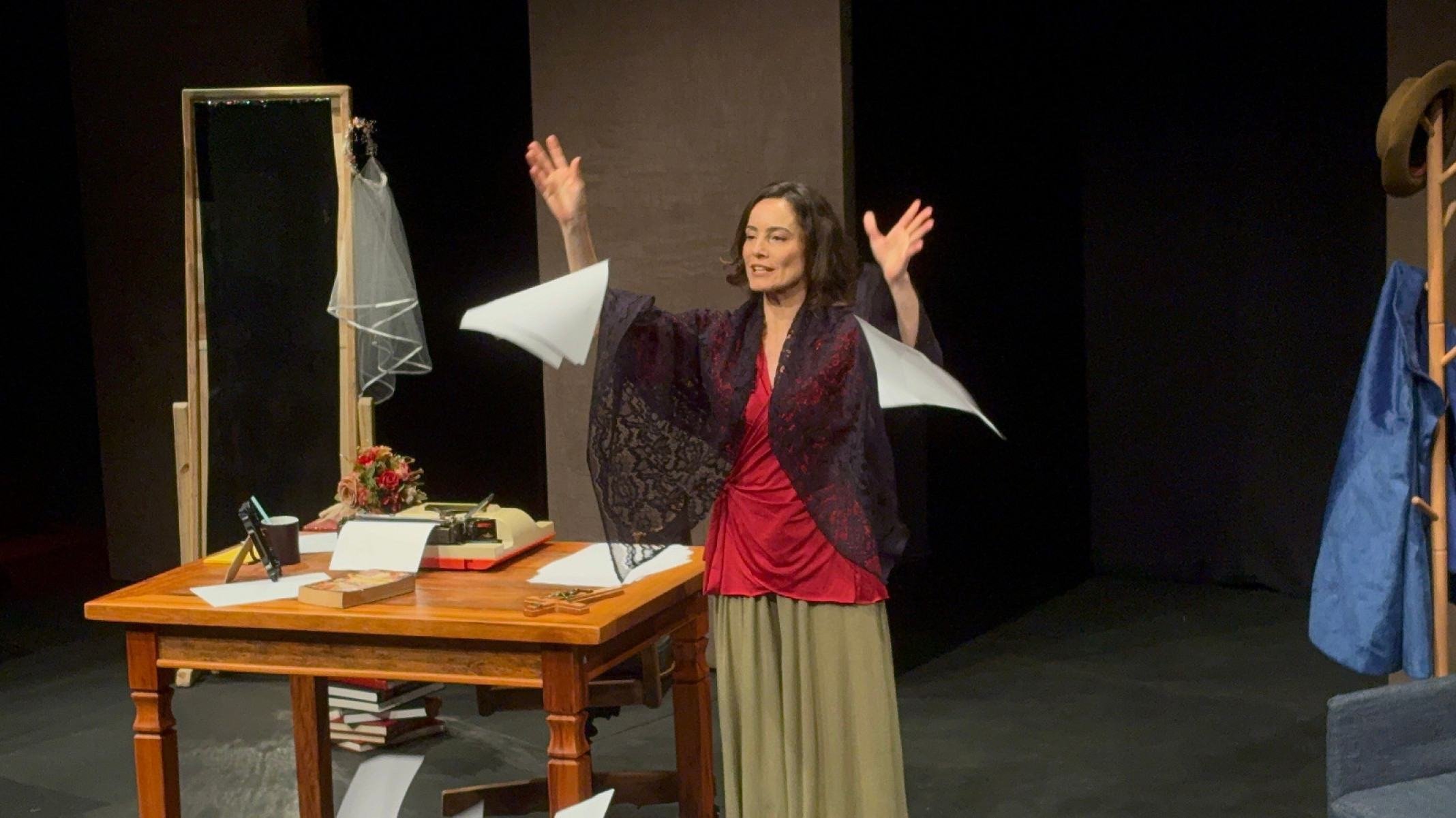 Atriz L&iacute;via Gaudencio tem as m&atilde;os para cima e folhas de papel voando atr&aacute;s dela durante ensaio da pe&ccedil;a Dona Doida, no palco do Teatro Cidade, em BH