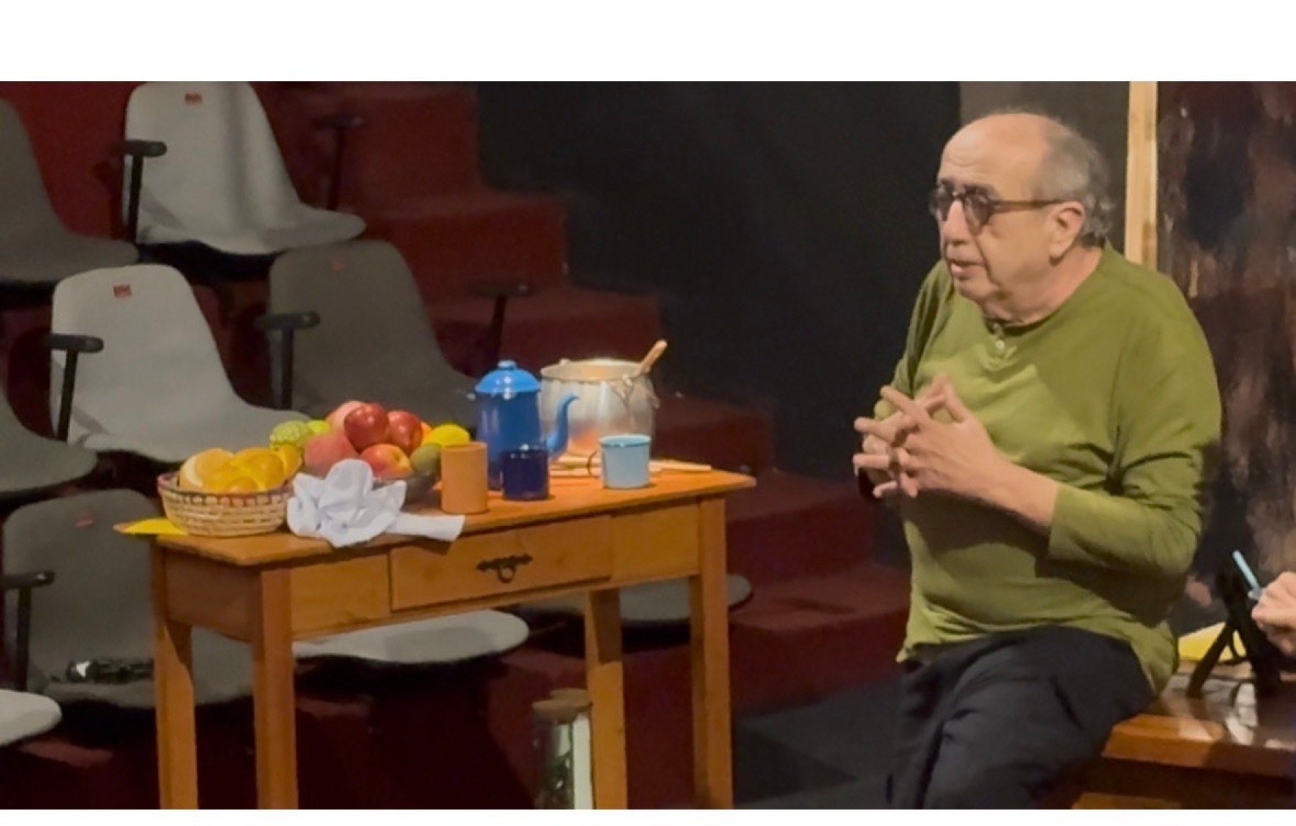 Diretor de teatro Pedro Paulo Cava est&aacute; sentado em mesa de cozinha com x&iacute;caras, bule e frutas, no cen&aacute;rio da pe&ccedil;a Dona Doida, no palco do Teatro da Cidade, em BH
