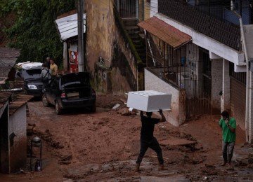 Morador carrega móvel na cabeça em rua enlameada de Juiz de Fora (MG), cidade atormentada pelas chuvas fortes há dias -  (crédito: Eduardo Anizelli/Folhapress)
