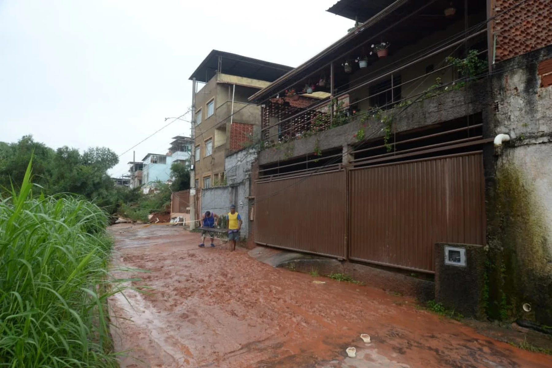 No bairro Jardim Natal, em Juiz de Fora, seis residências foram invadidas pela enchente. Pessoas limpam suas casas, removem móveis e utensílios, máquinas tentam desobstruir o leito do córrego que está repleto de destroços