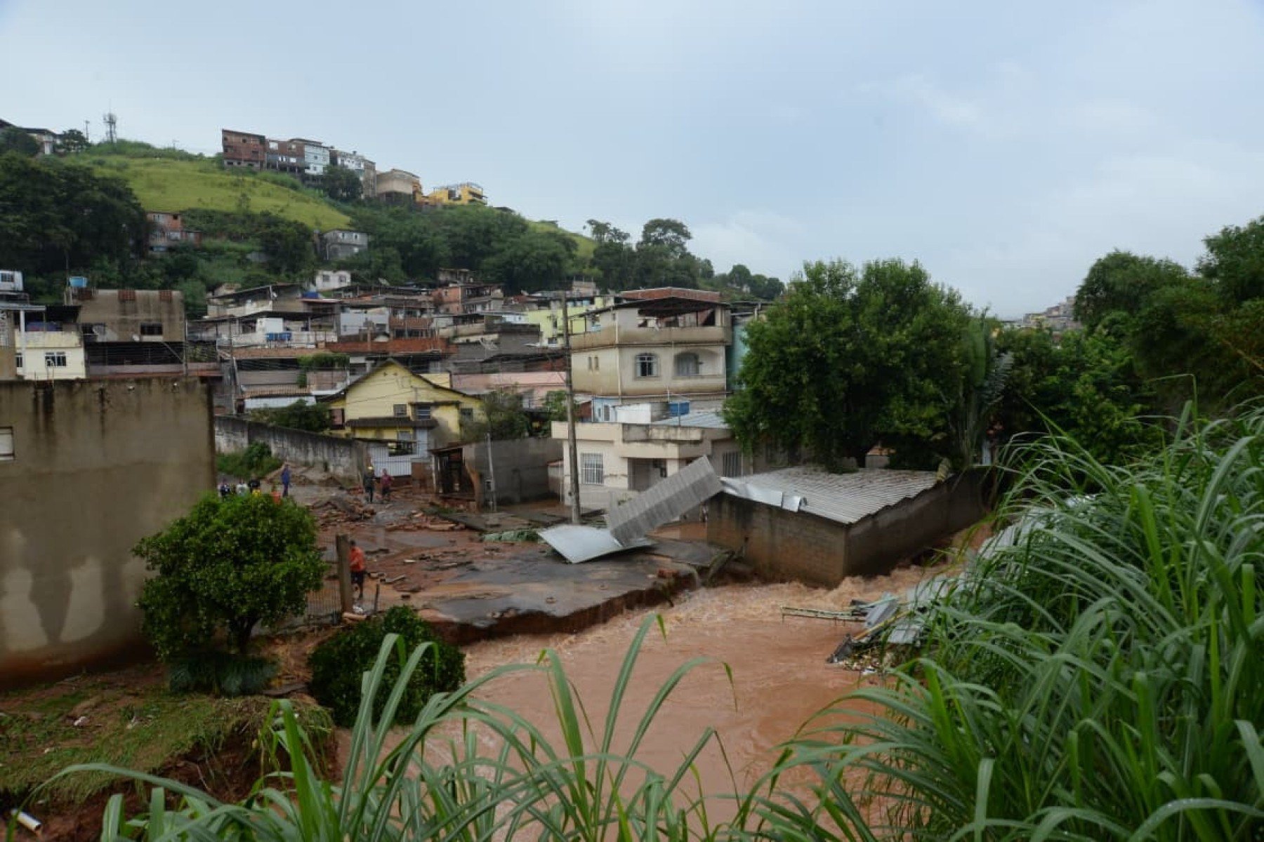 No bairro Jardim Natal, em Juiz de Fora, seis residências foram invadidas pela enchente. Pessoas limpam suas casas, removem móveis e utensílios, máquinas tentam desobstruir o leito do córrego que está repleto de destroços