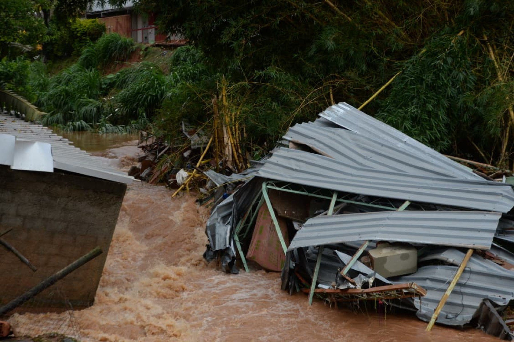 No bairro Jardim Natal, em Juiz de Fora, seis residências foram invadidas pela enchente. Pessoas limpam suas casas, removem móveis e utensílios, máquinas tentam desobstruir o leito do córrego que está repleto de destroços