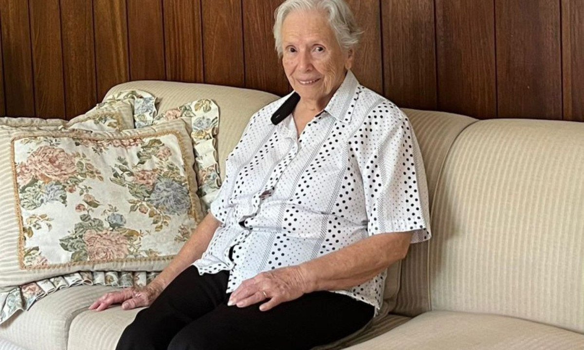 Nancy Guedes Junqueira, de 94 anos, sorri, sentada no sof&aacute; de sua casa, em Juiz de Fora