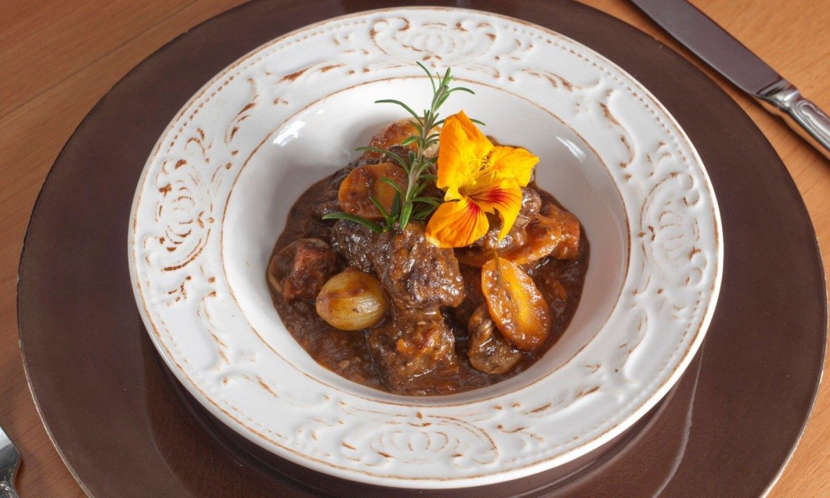 Bife bourguignon, com carne bovina e legumes, &eacute; servido em prato branco, visto de cima na foto