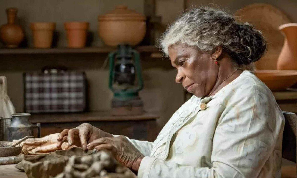 Zez&eacute; Motta est&aacute; de lado, de cabelos brancos, e costura em cena da novela A nobreza do amor