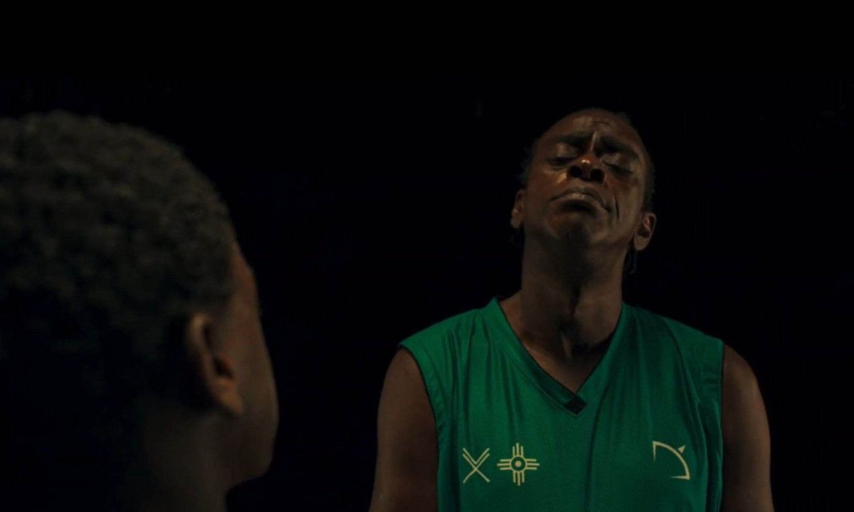 Seu Jorge encara com olhar desafiador menino que est&aacute; &agrave; sua frente, e de costas para a c&acirc;mara, em cena do filme Narciso