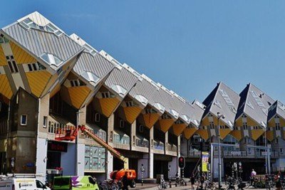 <p>As Casas Cubo de Rotterdam, criadas pelo arquiteto Piet Blom, formam um conjunto de residências inclinadas que parecem desafiar a lógica. Cada unidade é um cubo girado em 45 graus apoiado sobre um pilar hexagonal, criando uma paisagem urbana descrita como uma floresta geométrica.</p>
 -  (crédito: Zairon, CC BY-SA 4.0, via Wikimedia Commons)
