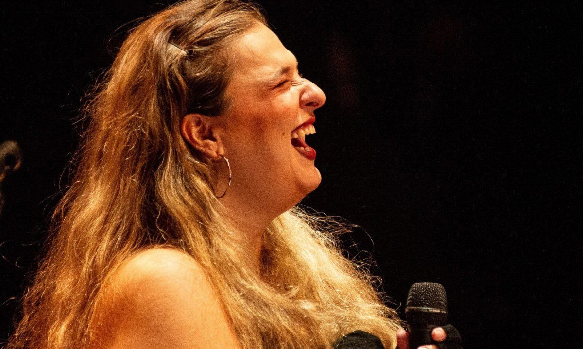 Alice Caymmi est&aacute; de perfil cantando e segurando o microfone durante show em BH