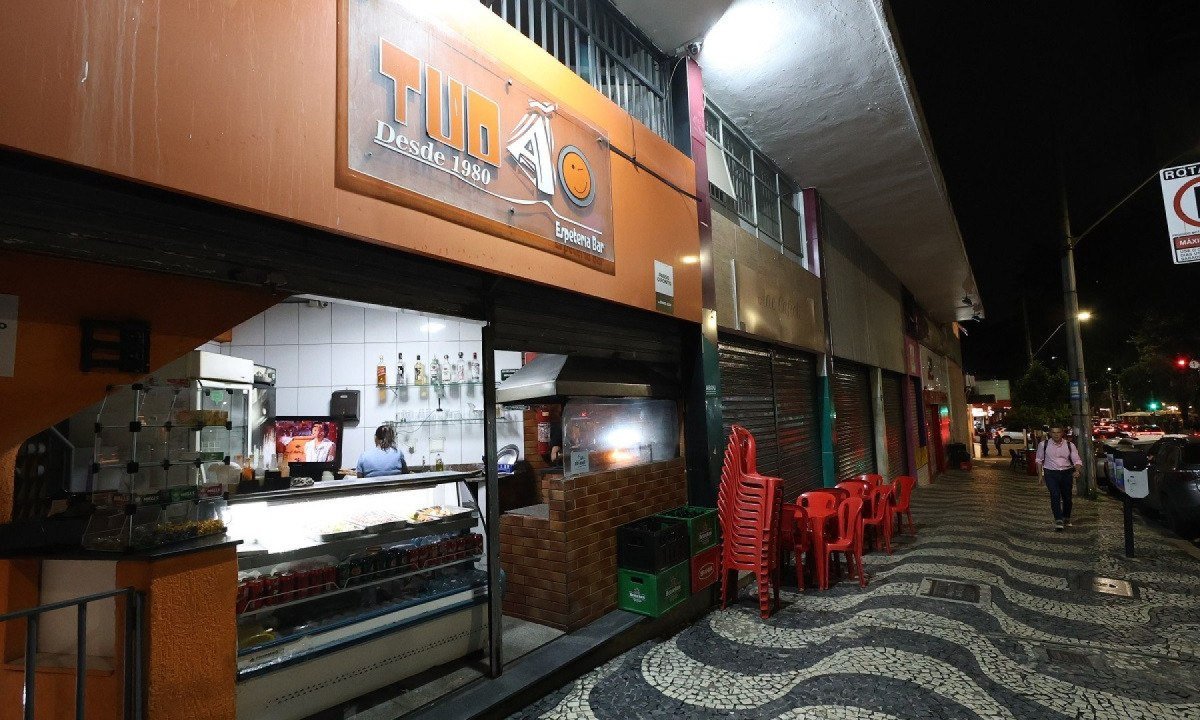Fachada da espeteria Tud&atilde;o, em Belo Horizonte; foto mostra a fachada do estabelecimento, com as portas abertas e mesas e cadeiras empilhadas sobre a cal&ccedil;ada