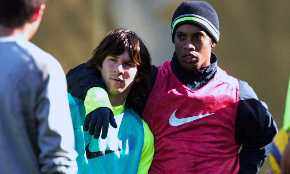 Messi, muito jovem, &eacute; abra&ccedil;ado por Ronaldinho Ga&uacute;cho, que veste o uniforme do Barcelona