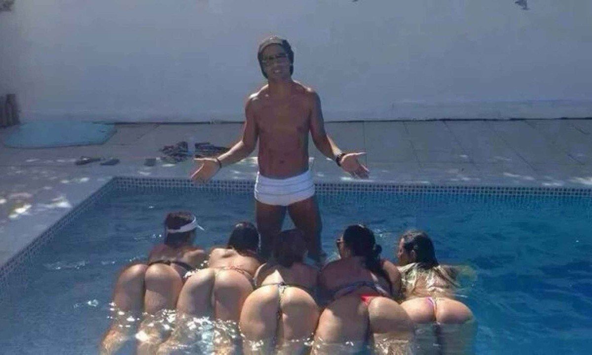 Ronaldinho Ga&uacute;cho, de sunga branca, est&aacute; em p&eacute; na piscina de sua casa, em Lagoa Santa. Deitadas na &aacute;gua, cinco mulheres exibem os traseiros para a c&acirc;mera
