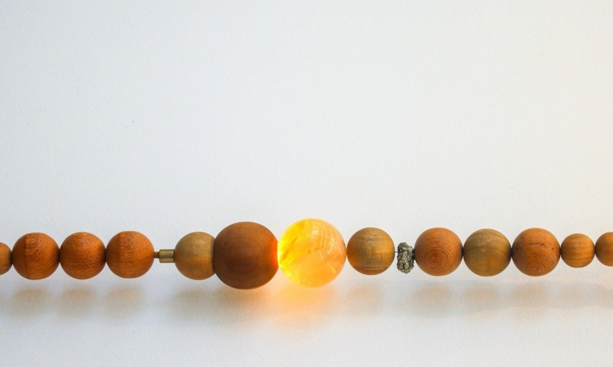 Detalhe da Lumin&aacute;ria Fluxo mostra fio de contas de cer&acirc;mica redondas e luz amarela saindo de conta maior, transparente