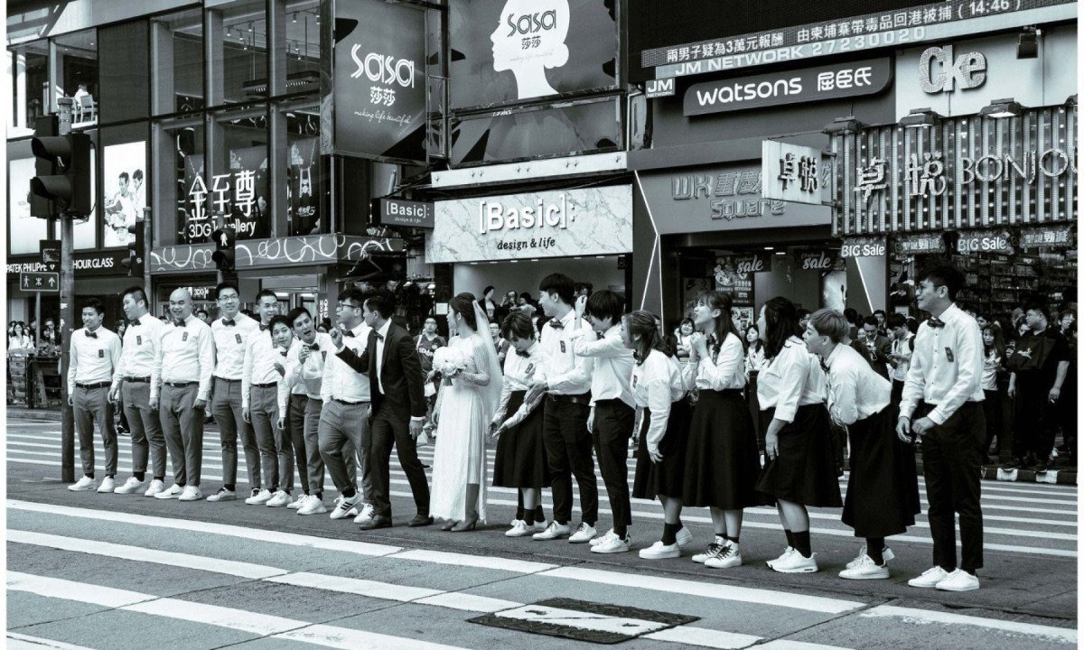 Homens, mulheres e noivos  asi&aacute;ticos sorriem e esperam para atravessar a rua em foto assinada por Marcelo Guelber G&oacute;es