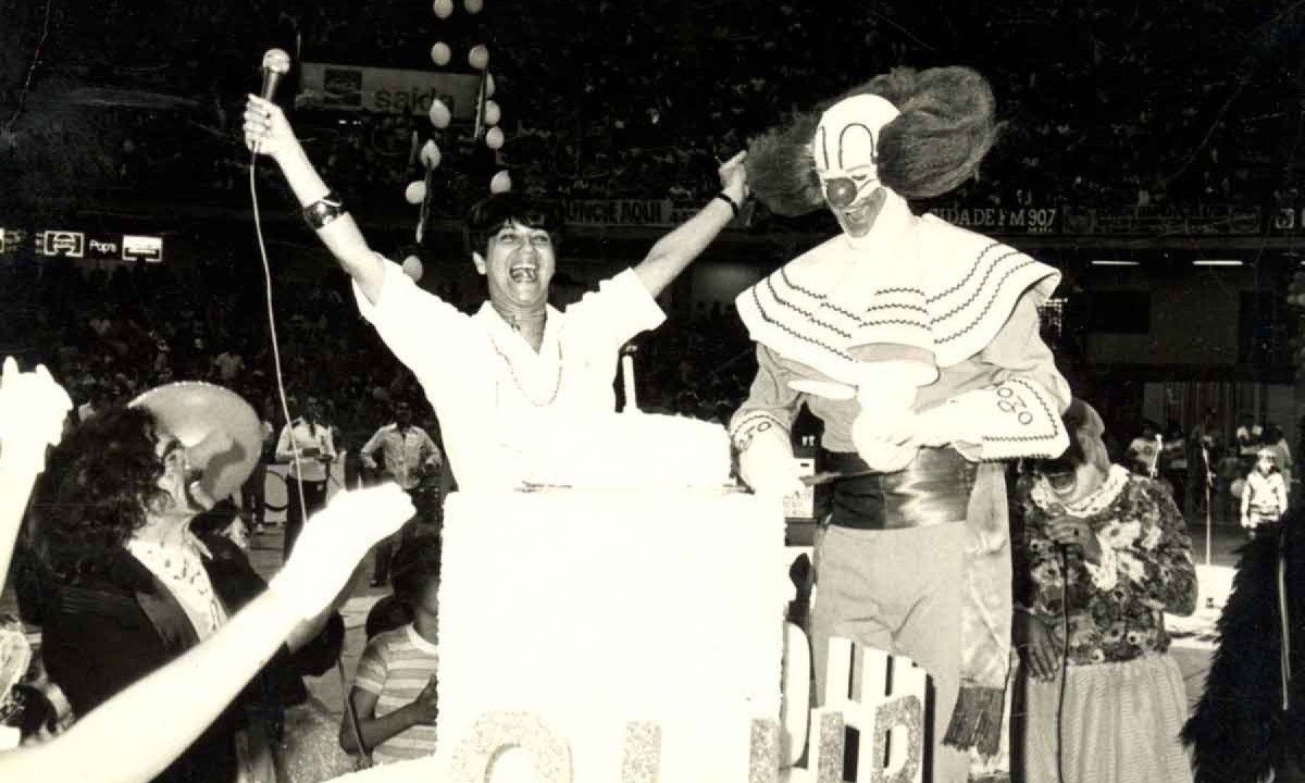 Apresentadora Tia Dulce sorri e ergue os bra&ccedil;os ao lado do palha&ccedil;o Bozo, no programa Clubinho, da TV Alterosa. Na frente e ao lado deles h&aacute; v&aacute;rias crian&ccedil;as sentadas no ch&atilde;o