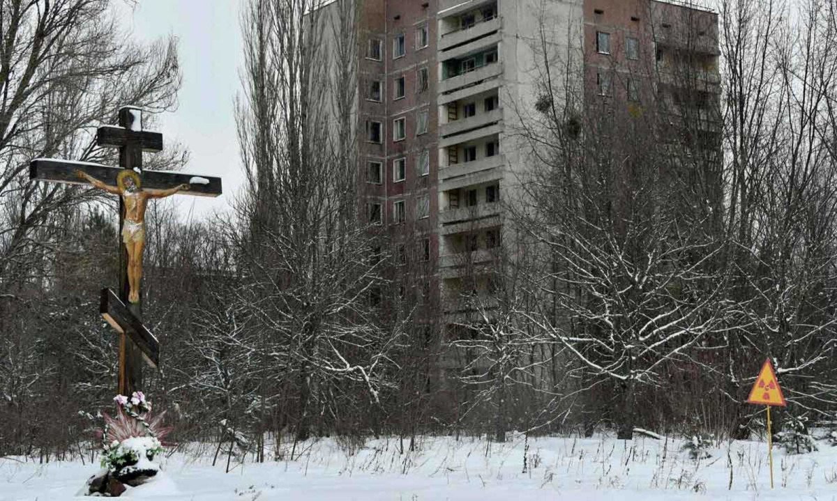 Entre a fé e o perigo - Um crucifixo se ergue diante do símbolo da radiação em Pripyat, um contraste que resume o que restou: a tentativa humana de encontrar sentido diante de um território ainda marcado pela ameaça invisível. Quarenta anos depois, o risco não desapareceu -  (crédito: AFP)