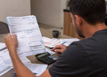 Homem segura boletos e faz contas para saber como vai pagar dívidas; Endividamento das famílias atinge 49,9% em fevereiro e renova recorde, mostra BC -  (crédito: imagem gerada por IA/acervo Estado de Minas)