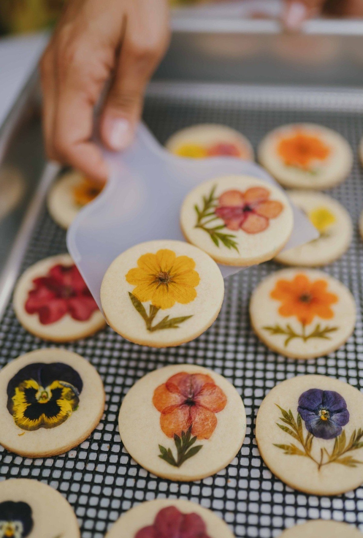 Por cima da massa amanteigada, s&atilde;o posicionadas flores comest&iacute;veis plantadas na casa da fundadora da Biscoito de Flor 