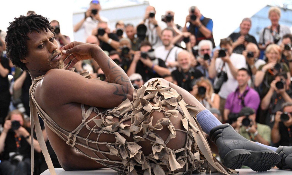 Usando vestido, ator brasileiro Jonathan Guilherme est&aacute; deitado sobre parapeito e posa para os fot&oacute;grafos no Festival de Cannes, em 2025