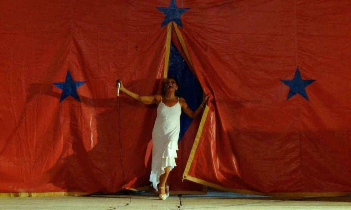 Atriz India Morena sai detr&aacute;s de cortina vermelha de circo sorrindo e usando vestido branco em cena do filme Mambembe