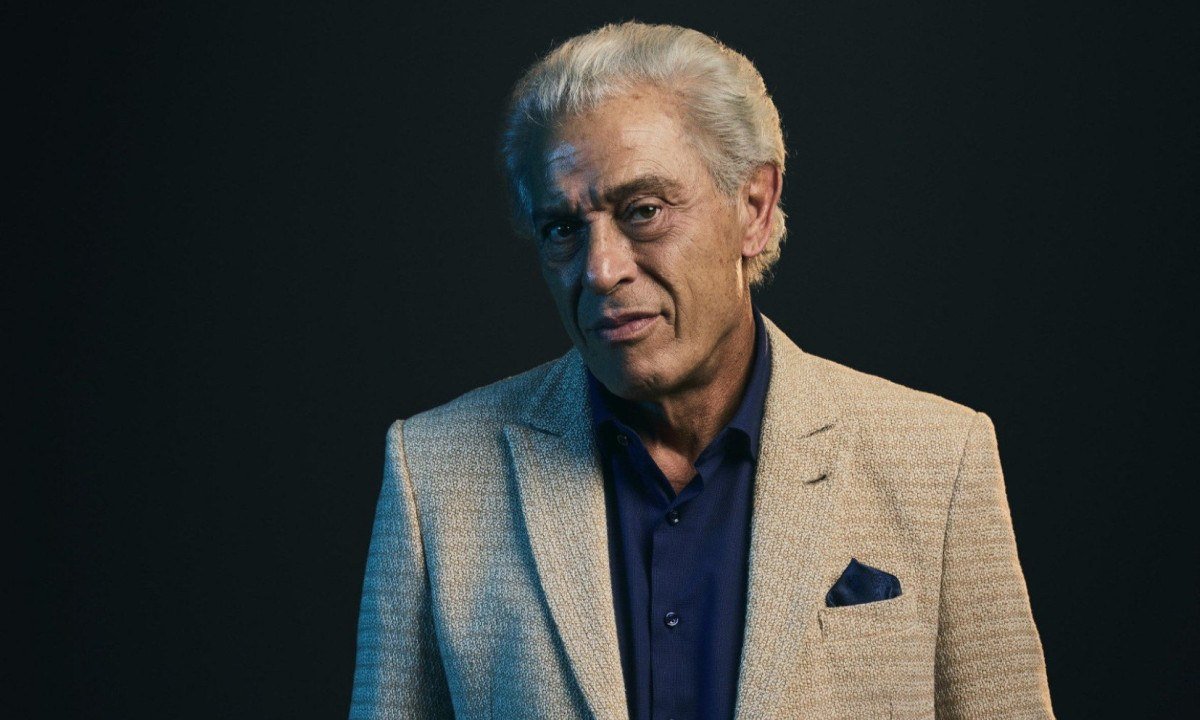 Ator Paulo Gorgulho veste casaco claro, blusa escura e olha para a c&acirc;mera